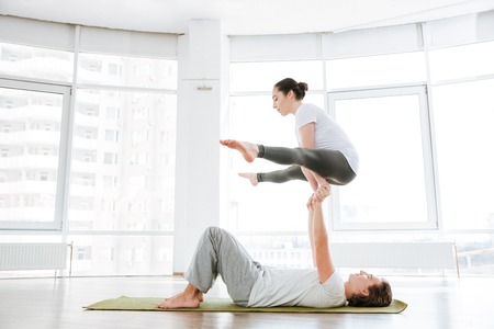 Concentrated man and woman doing acro yoga in pair in studio