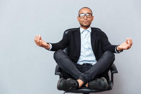 Closeup of attractive young man in glasses meditating on office chairの写真素材