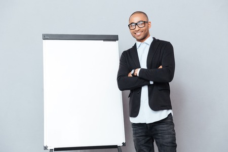 Smiling confident african man standing with arms crossed near flipchartの写真素材