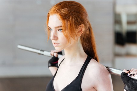 Close-up portrait of a young fitness girl doing exercises with barbell at the gym