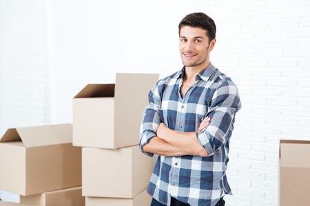 Happy handsome young man moving in and carrying carton boxesの写真素材