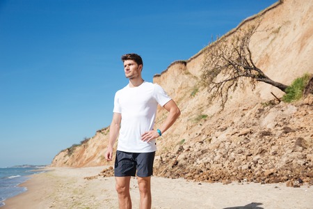 Portrait of thoughtful attractive young man standing on the beach and thinking