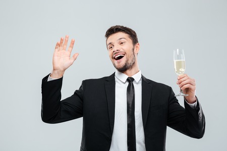 Happy excited young businessman holding glass of champagne and celebrating over white backgroundの写真素材