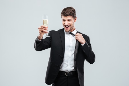 Relaxed happy young businessman with glass of chamagne standing and making cheers over white backgroundの写真素材