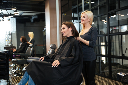 Young smiling girl sitting at the beauty salon and talking with female hairdresserの写真素材