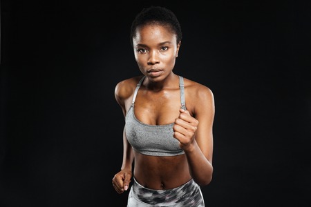 Close-up portrait of a sports african woman running isolated on a black backgroundの写真素材