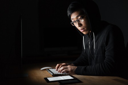 Hacker sitting and using laptop, tablet and smartphone in dark roomの写真素材