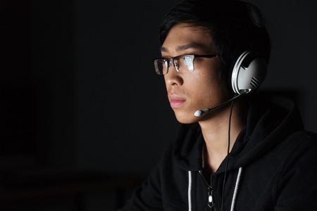 Portrait of handsome young man in glasses and headset in dark roomの写真素材
