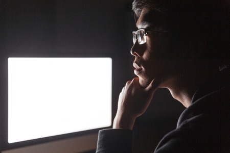 Pensive young man thinking and using blank screen computer in dark roomの写真素材