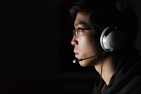 Profile of serious young man in glasses using headset in dark roomの写真素材