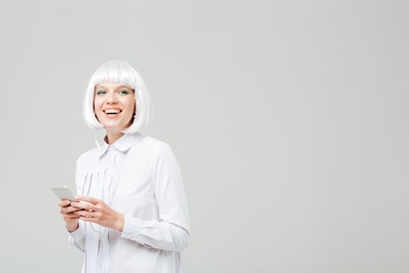 Cheerful charming young woman listening to music from mobile phone over white backgroundの写真素材