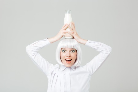 Funny playful young woman holding bottle of milk on her head over white backgroundの写真素材