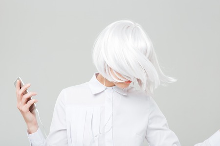 Attractive young woman with blonde hair listening to music from cell phone and dancing over white backgroundの写真素材