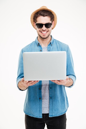 Cheerful attractive young man in sunglasses and hat holding laptopの写真素材