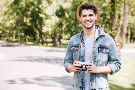 Happy atttractive young man in hat with old vintage photo camera outdoorsの写真素材
