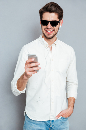 Portrait of a casual smiling man using smartphone isolated on a gray backgroundの写真素材