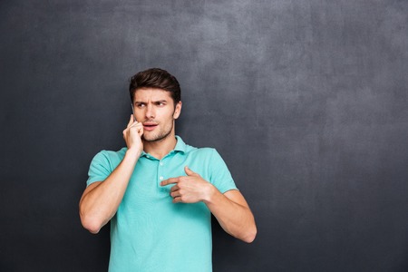 Confused handsome young man standing and talking on cell phone over chalkboard backgroundの写真素材
