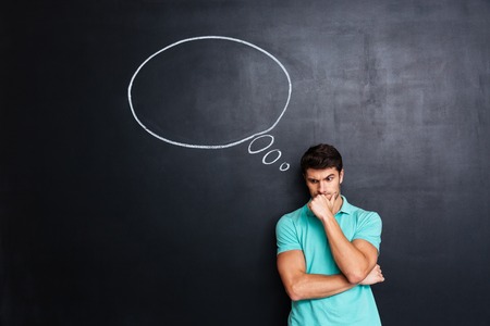 Serious stressed young man with hands folded thinking over chalkboard backgroundの写真素材