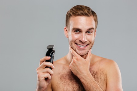 Smiling young handsome man holding razor over gray backgroundの写真素材