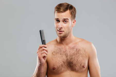 Cheerful young handsome man holding a comb isolated on the gray backgroundの写真素材
