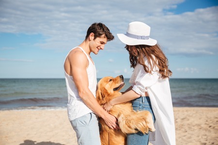 Young happy smiling couple in love sitting on the beach with dogの写真素材
