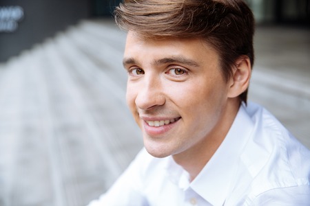 Closeup of smiling young businessman in white shirt sitting outdoorsの写真素材