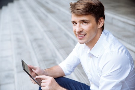 Portrait of happy handsome young businessman using tablet outdoorsの写真素材
