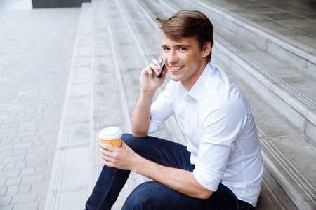 Smiling young businessman drinking coffee and talking on cell phone outdorsの写真素材