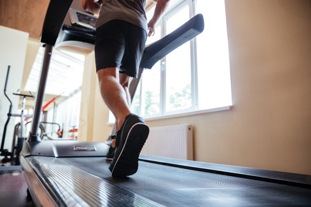 Back view of legs of young man athlete exercising and running on treadmill in gymの写真素材