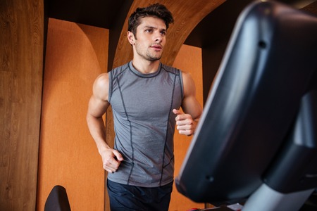 Serious young sportsman training and running on treadmill in gym