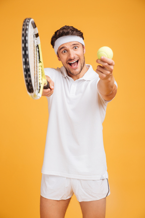 Happy young man tennis player inviting you to play over yellow backgroundの写真素材