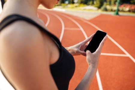 Cropped image of a beautiful woman resting after run and using smartphone on outdoor stadium