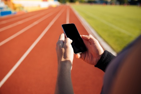 Cropped image of a handsome man resting after run and using smartphone on outdoor stadiumの写真素材