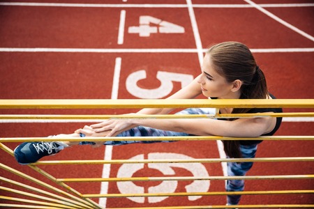 Portrait of a beautiful sports woman stretching legs on outdoor stadiumの写真素材