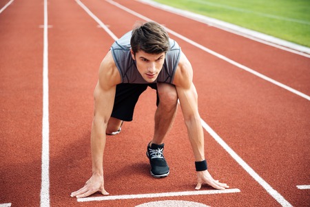 Portrait of the young muscular athlete at the start of the treadmill at the stadium