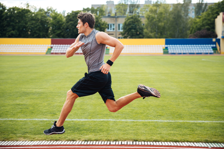 Side view of a young male athlete training on a race track at the stadiumの写真素材