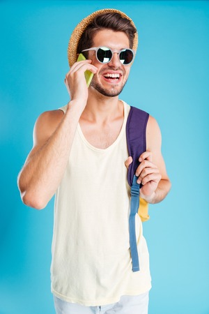 Smiling young man in hat and sunglasses with backpack talking on cell phoneの写真素材