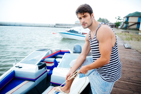 Handsome young sailor holding rope at the pier and looking at cameraの写真素材