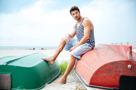 Handsome young man sitting on a fishing boat and looking away by the seaの写真素材