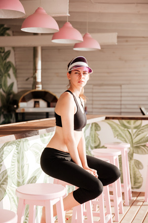 Young beautiful sports woman resting after workout at the beach cafe and looking at cameraの写真素材