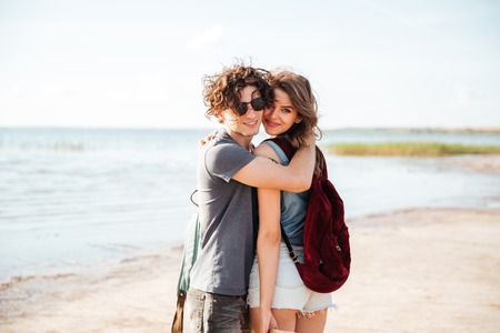 Beautiful young couple with backpacks standing and hugging on the beachの写真素材