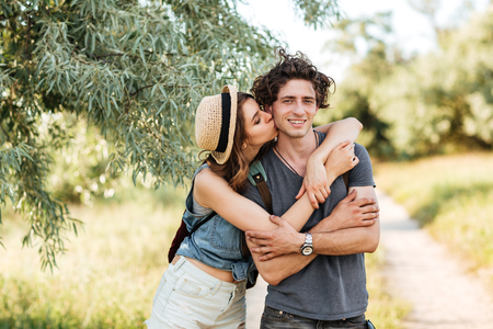 Young attractive hipster couple standing against trees on the background kissing and huggingの写真素材
