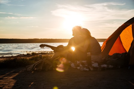 Silhouette of happy young couple sitting near touristic tent and huggingの写真素材