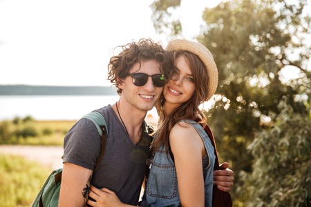 Portrait of smiling young hipster couple standing against trees and sea on the backgroundの写真素材