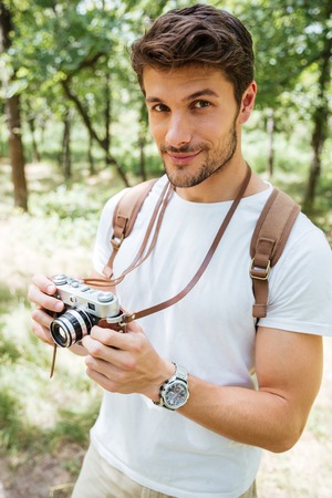 Handsome young man with backpack taking photos with old photo camera in forestの写真素材