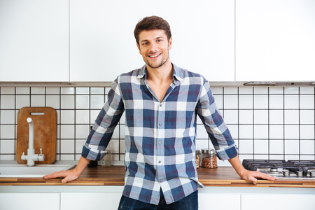 Cheerful young man in checkered shirt standing on the kitchenの写真素材