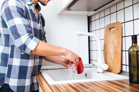 Closeup of young man in checkered shirt washing dishes on the kitchenの写真素材