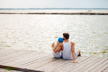 Loving couple on the beach hugging while sitting and looking at the seaの写真素材