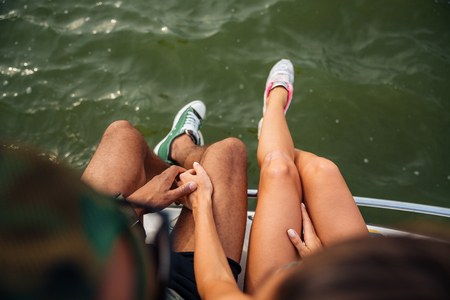 Top view of legs of young couple in sneakers sitting near the seaの写真素材