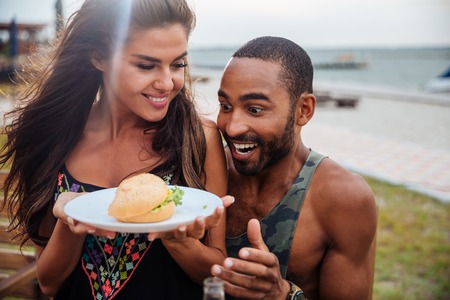 Young afro man looking hungry and looking at the burger on a plateの写真素材